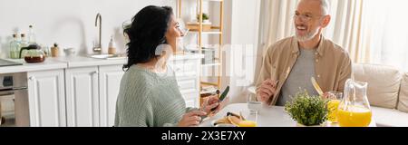 Eine behinderte Frau im Rollstuhl und ihr Mann stehen zusammen in einer gemütlichen Küche zu Hause, umgeben von Kochutensilien. Stockfoto