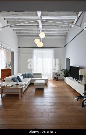Vorderansicht eines modernen Wohnzimmers mit einem großen Ledersofa, Fernseher auf Medienkonsole und weißem Vorhangfenster in einer renovierten Wohnung Stockfoto
