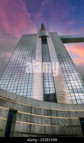 Die Pracht eines Art déco-Wolkenkratzers wird vor der Leinwand eines dramatischen Sonnenuntergangs verwundert. Das reflektierende Glas des Gebäudes fängt das verblassende Licht ein, während architektonische Details sich in den leuchtenden Farben der Dämmerung abheben. Dieses Bild feiert die Kreuzung von historischem Design und Naturschauspiel. Art déco-Wolkenkratzer erhebt sich vor einem dramatischen Sonnenuntergangshimmel. Hochwertige Fotos Stockfoto