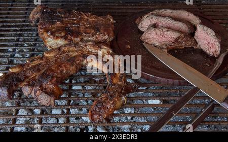 Argentinisches Barbecue. Einige ausgezeichnete Stücke argentinisches Rindfleisch auf einem Holzkohlegrill und einem Holztisch mit Messer. Nahaufnahme der geschnittenen gegrillten Be Stockfoto