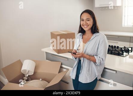 Porträt, asiatische Frau und glücklich zu Hause mit Kartons zum Auspacken, zufrieden und selbstbewusst mit Besitz. Immobilien, Lächeln und Möbel in der Küche Stockfoto