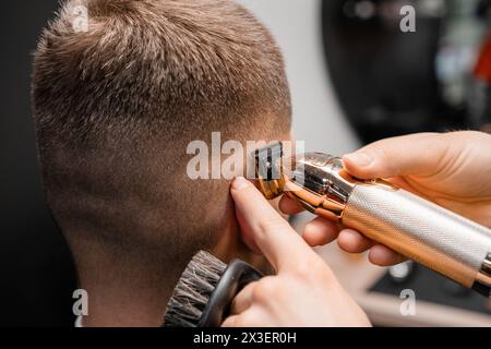 Friseur rasiert männliche Kundenhaare mit scharfem Trimmer in der Nähe des Friseurshops. Ein erfahrener Friseur schneidet im Friseursalon Männerhaare auf dem Hinterkopf mit einer Maschine Stockfoto