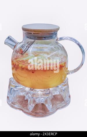 Glas-Teekanne mit fruchtigem Zitronen-Sanddorn-Tee auf einem wärmenden Stand isolieren auf einem weißen Hintergrund Nahaufnahme. Stockfoto