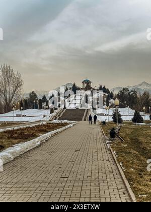 Ein Paar läuft an einem nebeligen Wintertag einen Steinweg des Parks entlang, mit einem Gebäude und Bäumen im Hintergrund. Stockfoto