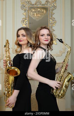 Zwei Frauen in schwarzen Ständen mit Saxophonen im barocken Studio mit Spiegel Stockfoto