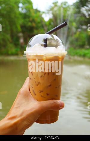 Hand hält eine Tasse leckeren thailändischen Eistees mit Brunnen im Hintergrund Stockfoto