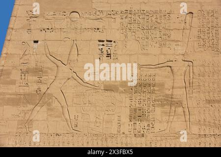 Relief des ägyptischen Pharao Ramses III., der Feinde tötet, und des Gottes Amun, das auf dem ersten Pylon von Medinet Habu auf der Westbank von Luxor, Ägypten, gemeißelt wurde Stockfoto