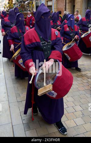 Tarragona, Spanien - 26. April 2024: Maskierte Teilnehmer spielen Schlagzeug und schaffen eine feierliche und spirituelle Atmosphäre. Stockfoto