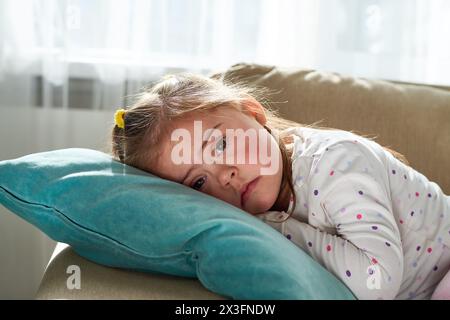 Porträt eines süßen kleinen Mädchens mit Down-Syndrom, das auf dem Kissen liegend in die Kamera blickt Stockfoto