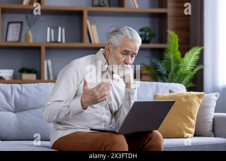 Verärgerter, ranghaariger Mann, der mit Familie und Bank telefoniert, auf dem Sofa sitzt und finanzielle Probleme und Fragen löst. Stockfoto