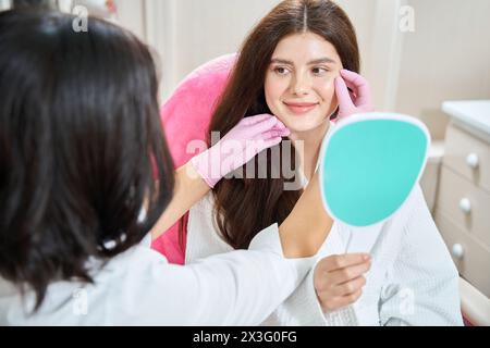 Fröhliche junge Frau, die sich einer Gesichtshaut-Untersuchung in der Schönheitsklinik unterzieht Stockfoto