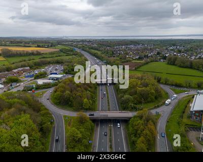 Drohnenaufnahme, die eine geschäftige Autobahnkreuzung mit üppigen grünen Feldern und Stadträndern erfasst Stockfoto