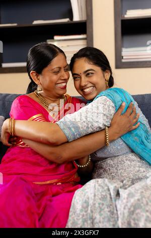 Indische Mutter und Teenager-Tochter in traditioneller Kleidung, lachen und umarmen zu Hause Stockfoto