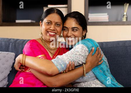 Indische Mutter und Tochter im Teenageralter tragen traditionelle Kleidung und umarmen sich zu Hause Stockfoto