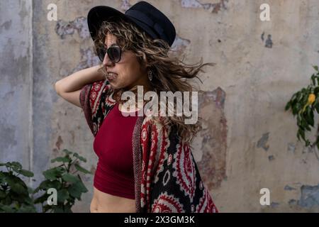 Junge lateinamerikanische Frau mit lockigem Haar, Hut, Sonnenbrille und roter Kleidung. Stockfoto