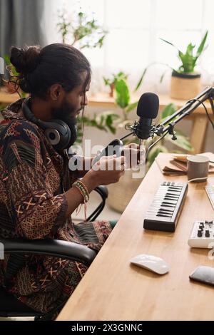 Junger kreativer Mann, der am Arbeitsplatz im Heimstudio sitzt und Tonaufnahmegeräte repariert, bevor er neue Musik kreiert oder aufführt Stockfoto