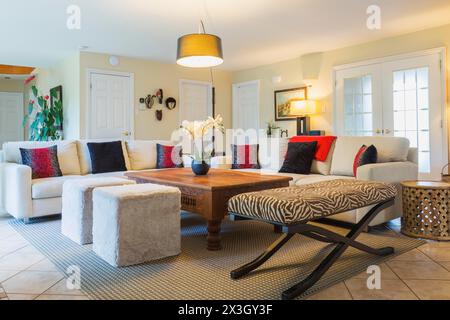 Beigefarbene gepolsterte Sofas mit bunten Kissen, hölzerner Couchtisch und Ottomane mit Zebramotiv im Wohnzimmer in einem luxuriösen Wohnhaus Stockfoto