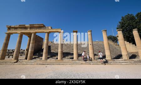 Touristen besuchen an einem sonnigen Tag alte Ruinen mit Säulen unter einem klaren blauen Himmel, Akropolis von Lindos, Morgenlicht, Propyläen mit Treppe Stockfoto