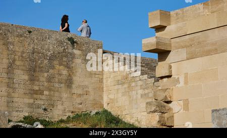 Zwei Leute, die auf einer alten Mauer stehen und sich unterhalten, Akropolis von Lindos, Morgenlicht, Lindos, Rhodos, Dodekanesisch, Griechische Inseln Stockfoto