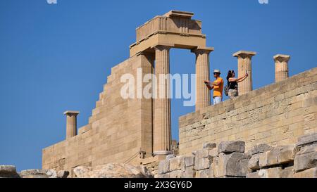 Touristen sehen die majestätischen Säulen einer antiken Ruine unter einem klaren blauen Himmel, Akropolis von Lindos, Morgenlicht, Tempel von Athena Lindia, Lindos Stockfoto