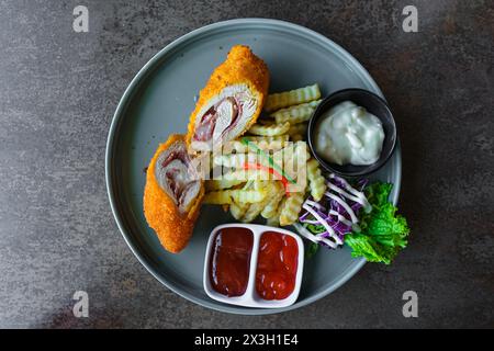 Panierte Fleischbrötchen mit Crinkle geschnittenen Pommes frites, Gemüse und drei Arten von Saucen: Cremige Soße, Ketchup und Tatar. Flacher Lagewinkel. Stockfoto