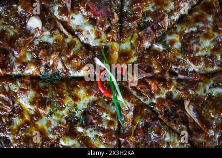 Pizza mit goldbrauner Kruste und dunkler Textur, geschmolzenem Käse, einer einzelnen roten Chilischote und Belägen wie Peperoni und Kräutern Stockfoto