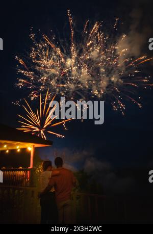 Junger afroamerikanischer Mann umarmt seine weiße Freundin, während er vom Aussichtsplattform über dem Fluss aus Feuerwerk am 4. Juli beobachtet Stockfoto