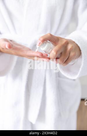 Eine junge kaukasische Frau in weißem Gewand, die zu Hause Lotion auf die Hände aufträgt, Kopierraum Stockfoto