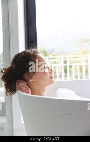 Eine junge kaukasische Frau, die sich zu Hause in der Badewanne entspannt, die Augen schließen Stockfoto