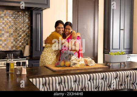 Indische Mutter und Teenager-Tochter, umarmt zu Hause in der Küche Stockfoto