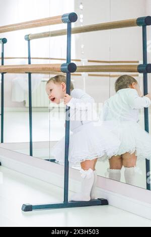 Porträt einer niedlichen Ballerina, die neben der Ballettstange sitzt und Schuhe anzieht Stockfoto