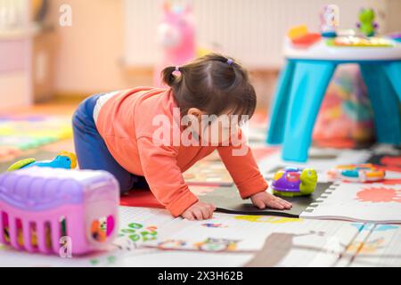 Das kleine Mädchen spielt allein mit ihren Spielzeugen. Baby steht in ihrem Zimmer voller Spielzeug Stockfoto