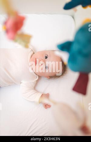 Niedliches Baby Baby Baby Baby steht in ihrem Bett und schaut auf das hängende Spielzeug Stockfoto