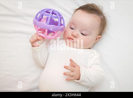 Niedliches Mädchen Kleinkind steht auf dem Rücken in der Krippe und spielt mit einem sensorischen Spielzeug Stockfoto