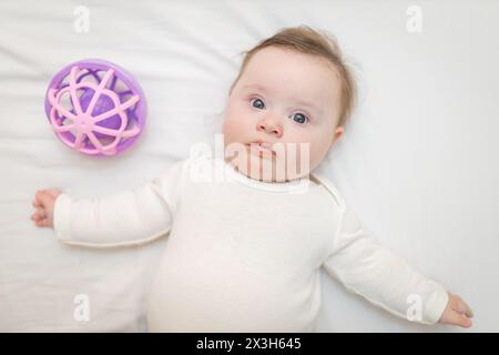 Niedliches Baby Baby Baby Baby steht auf dem Rücken in der Krippe neben einem sensorischen Spielzeug Stockfoto