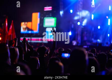 Begeistertes Publikum beim abendlichen Musikfestival mit erhobenen Händen, hellen Bühnenlichtern, Live-Performance-Energie, Outdoor-Konzert-Vibe und Beats-Fans Stockfoto