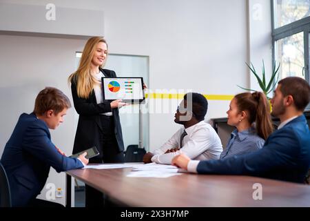 Weibliche CEO präsentiert Kollegen aus verschiedenen Ethnien während des Meetings farbenfrohe Diagramme auf dem Laptop. Männliche, weibliche Mitarbeiter führen Strategiediskussionen durch, Afrikaner Stockfoto