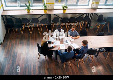 Draufsicht einer vielfältigen Gruppe von Fachleuten in einer Besprechung. Eine Geschäftsführerin führt eine Unternehmensberatung an einem modernen Bürotisch mit multiethnischen Personen Stockfoto