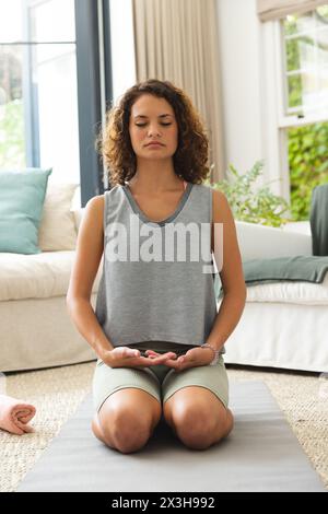 Eine junge kaukasische Frau, die zu Hause in einem ruhigen Wohnzimmer meditiert Stockfoto