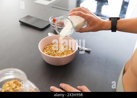 Zu Hause, Kaukasierin, die Milch in Getreide gießt, Smartphone in der Nähe Stockfoto