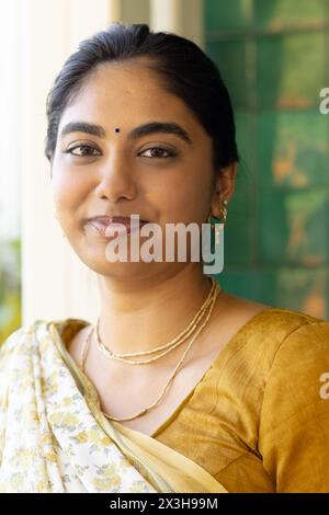 Zu Hause, eine junge indische Frau in rotem Kleid mit goldener Stickerei, stehend und lächelnd Stockfoto