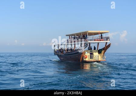 Khasab, Oman - 1. Januar 2024: Eine traditionelle hölzerne Dhow voller Touristen segelt sanft durch die ruhigen Gewässer der Fjorde von Khasab. Stockfoto