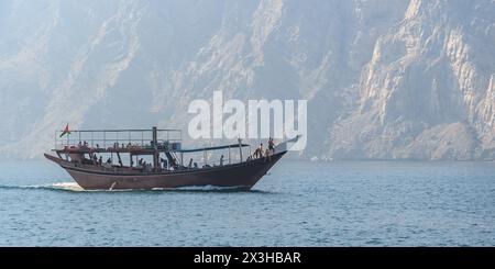 Khasab, Oman - 1. Januar 2024: Touristen an Bord eines traditionellen omanischen Bootes erkunden die ruhigen Fjorde von Khasab, umgeben von majestätischen felsigen Bergen. Stockfoto