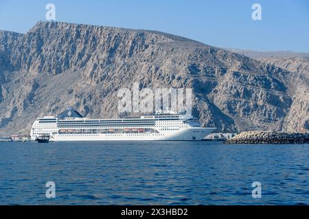 Khasab, Oman - 1. Januar 2024: Ein majestätisches weißes Kreuzfahrtschiff legt in der Nähe der zerklüfteten Berge an und bietet eine harmonische Mischung aus natürlicher Schönheit und Huma Stockfoto