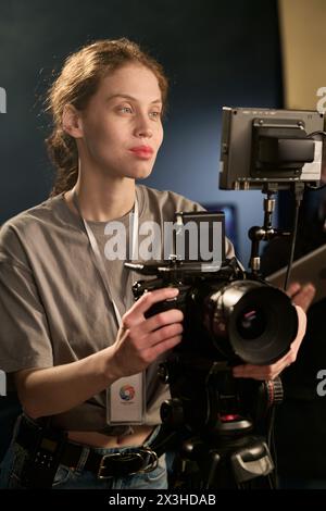 Vertikales Porträt einer lächelnden kaukasischen Kamerafrau, die während der Videoproduktion Geräte am Set bedient Stockfoto