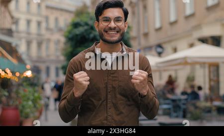 Glücklicher lächelnder enthusiastischer indischer arabischer männlicher Mann Mann Geschäftsmann mit Blick auf die Kamera positiver Gewinner freut sich über den Sieg, der Glück feiert Stockfoto
