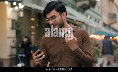 Glücklicher hoffnungsvoller indischer arabischer ethnischer Mann Mann Geschäftsmann männlicher junger Student hält Handy-Smartphone und wünscht Hoffnung betend gekreuzt Stockfoto