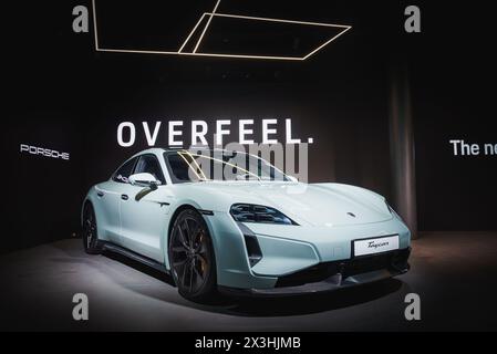 Hellblauer Porsche Taycan auf der Autoshow mit OVERFEEL-Schriftzug im dunklen Raum. Stockfoto