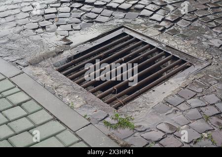 Wasser fließt an einem fließenden Tag durch die Mannlochabdeckung Stockfoto