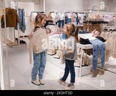 Zwei Mädchen teilen sich einen lustigen Moment, während sie in einem Bekleidungsgeschäft über ein neues Kleidungsstück nachdenken. Stockfoto